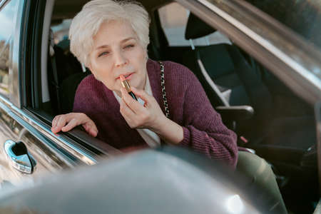 Female car passenger putting on make-up before the side mirrorの写真素材