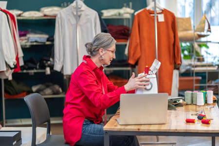 Woman touching sewing machine sitting sideways to camera