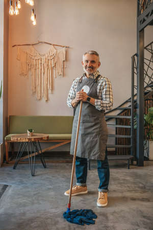 Man holding mop smiling at camera in cafeの写真素材