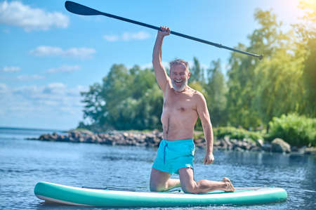 Energetic man with raised paddle kneeling on sapboardの写真素材