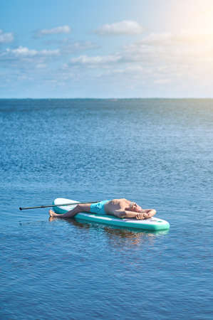Man lying drifting on paddling board on waterの写真素材