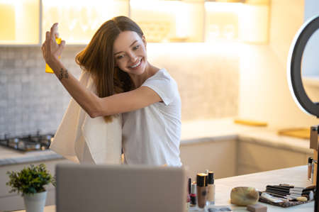 Woman holding spray near hair looking at laptopの写真素材