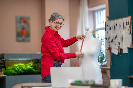 Smiling woman touching mannequin with measure