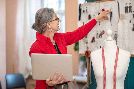 Woman holding laptop touching sketch on wallの写真素材