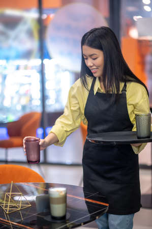 Smiling woman lowering glass of cappuccino on tableの写真素材