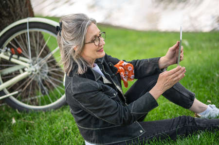 A woman with a tablet sitting near the river and restingの写真素材
