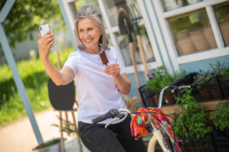 Cheerful woman on a bike eating ice-cream and looking happy