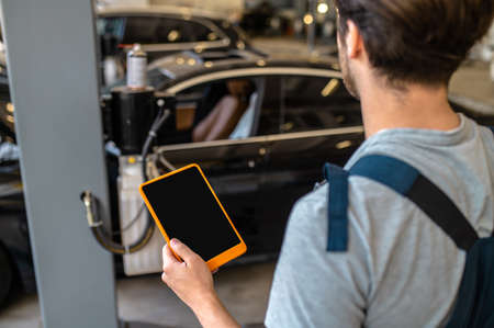 Mechanic with tablet back to camera looking at carの写真素材