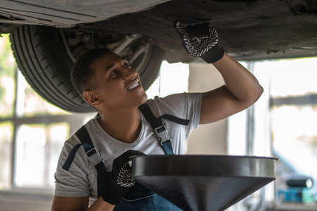 Cheerful young mechanic inspecting the vehicle underbodyの写真素材