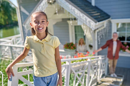 Cute girl standing near the house and smiling, dad looking at herの写真素材