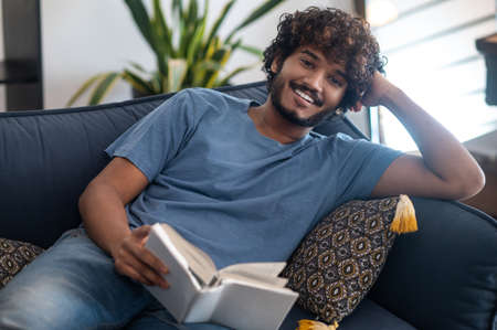 A young man reading a book while lying on the sofa