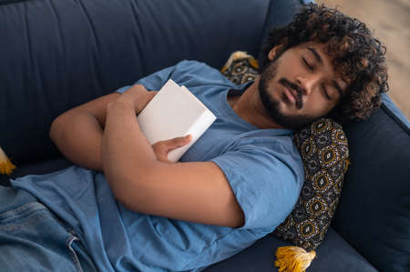 Young man sleeping on the sofa with a book in hands