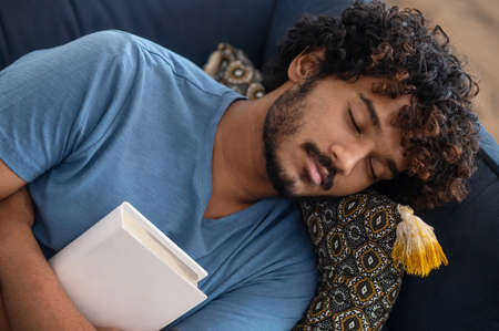 Young man sleeping on the sofa with a book in hands