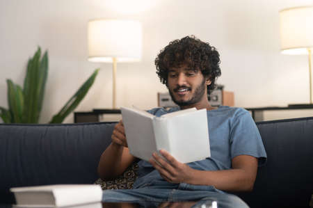 Curly-haired indian guy reading a book and looking involved