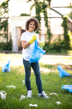 Curly-haired teen gathering garbage in the parkの写真素材