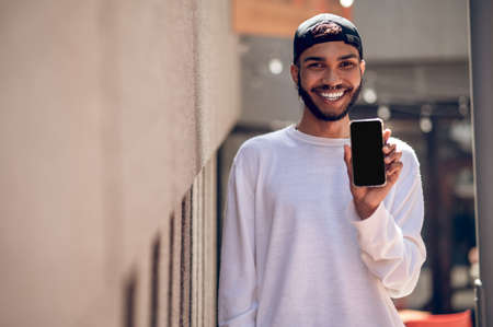 Handsome man in a black cap with a smartphone in the streetの写真素材
