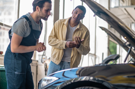 Customer looking questioningly at mechanic near hood of car