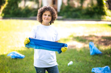 Teen in white thsirt standing on the grass among plastic bottlesの写真素材