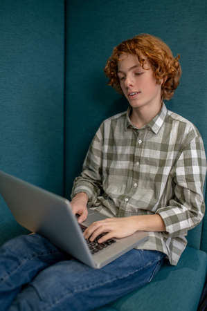 Ginger boy sitting with a laptop and watching something online