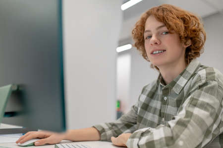 A ginger schoolboy sitting at the computer at school and looking involved