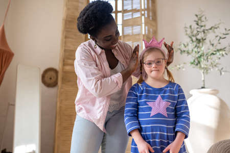 African american woman putting a crown on head of a girl in blue dressの写真素材