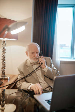 A gray-haired gentleman calling to the room serviceの写真素材