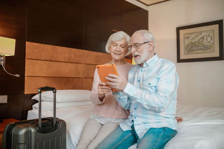 Senior couple sitting on a bed and watching something on a taletの写真素材
