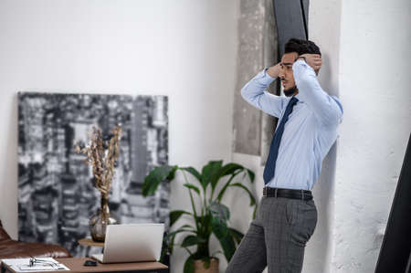 Sad man touching head standing sideways to cameraの写真素材