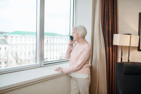 Elderly lady near the window with a smartphone in handの写真素材