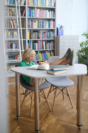 Joyous schoolboy using his smartphone in the reading room