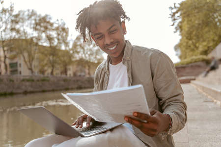 Guy looking at papers working on laptop outdoors