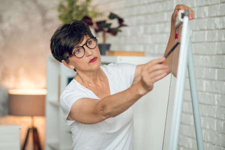Mature dark-haired woman standing near the flipchart and working on project details