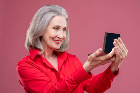 Mature woman in red doing makeup and looking contentedの写真素材
