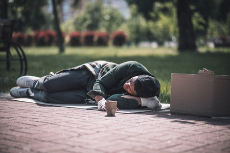 Dark-skinned man sleeping on ground in parkの写真素材
