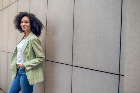 Pretty curly-haired woman standing near the wall in the streetの写真素材