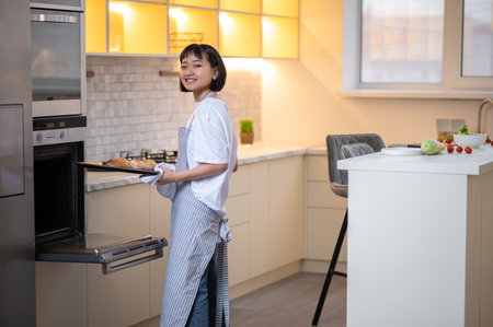 Young housewife baking something in the oven and looking busyの写真素材