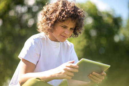 Focused adolescent looking at the gadget in his handsの写真素材