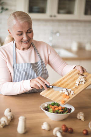 A blonde woman in apron in the kitchen looking busyの写真素材