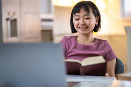 A girl in violet tshirt sitting at the laptop and looking happyの写真素材