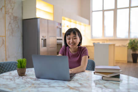 A girl in violet tshirt sitting at the laptop and looking happy