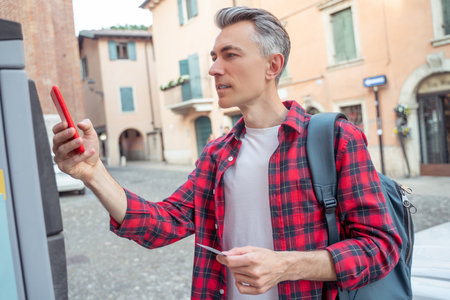 Mid aged man in a plaid shirt standing with a phone near atmの写真素材