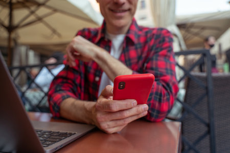 Mid aged man in plaid shirt sitting at the table in the street cafe with a phone in handsの写真素材