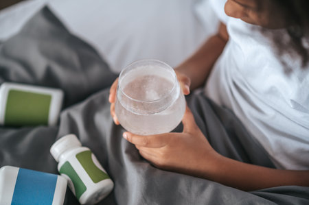 A girl taking a pill while lying in bed and feeling unwellの写真素材