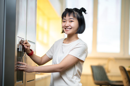 Cheerful female filling a glass with water from the fridge