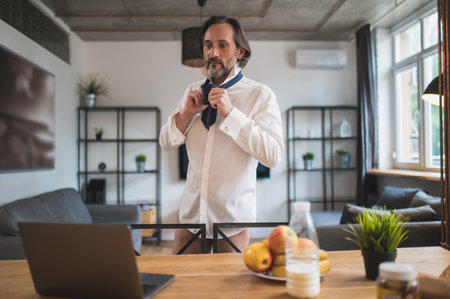 Bearded man putting on a shirt and a tie before the video callの写真素材