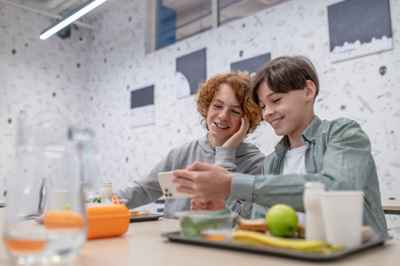 Two cheerful schoolmates sitting in the school canteenの写真素材