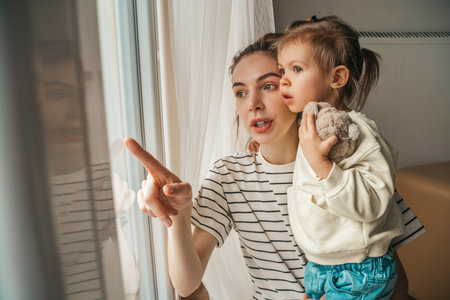 Focused mother and her daughter looking out of the windowの写真素材