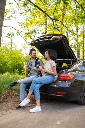 Young people sitting on the car boot and eating their lunchの写真素材