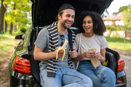 Young people sitting on the car boot and eating their lunchの写真素材