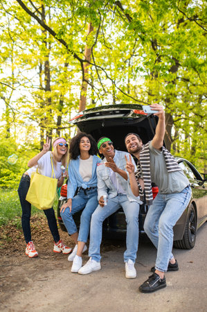 Group of friends making selfie in the forest while sitting on the car bootの写真素材